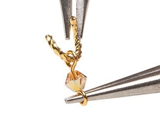 Twisted jump ring is being inserted through one side of the drop created in Step 1